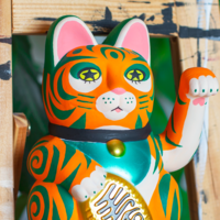 A painted lucky cat, it is orange with green stripes and stars in it's eyes.