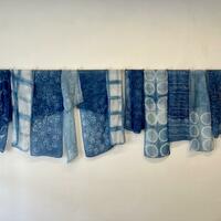 Row of blue silk scarves dyed with indigo, showing patterns in white. 