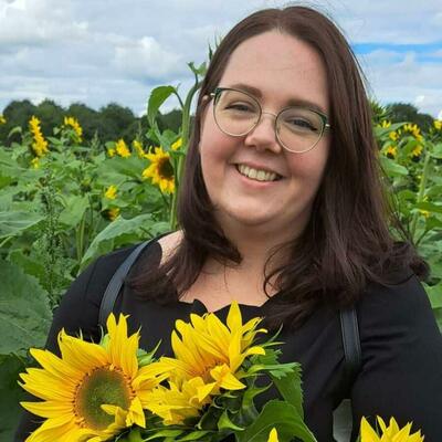 Image of Jenna Kelly the artist in a sunflower field holding sunflowers. 