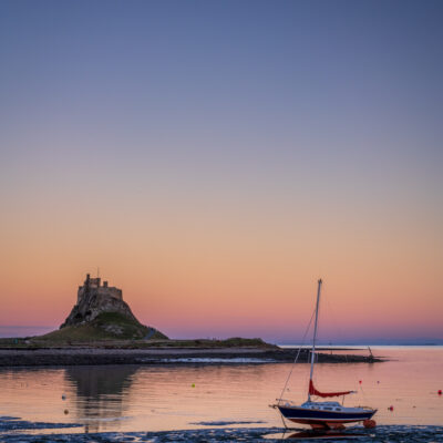 Stuart Feurtado: Lindisfarne Abbey seen against evening light with a yatch in the foreground