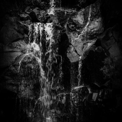 Stuart Feurtado: Black and white image of a waterfall with a face appearing in the rock formation beside it.